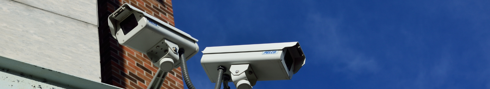 Two wall-mounted CCTV cameras against a blue sky backdrop