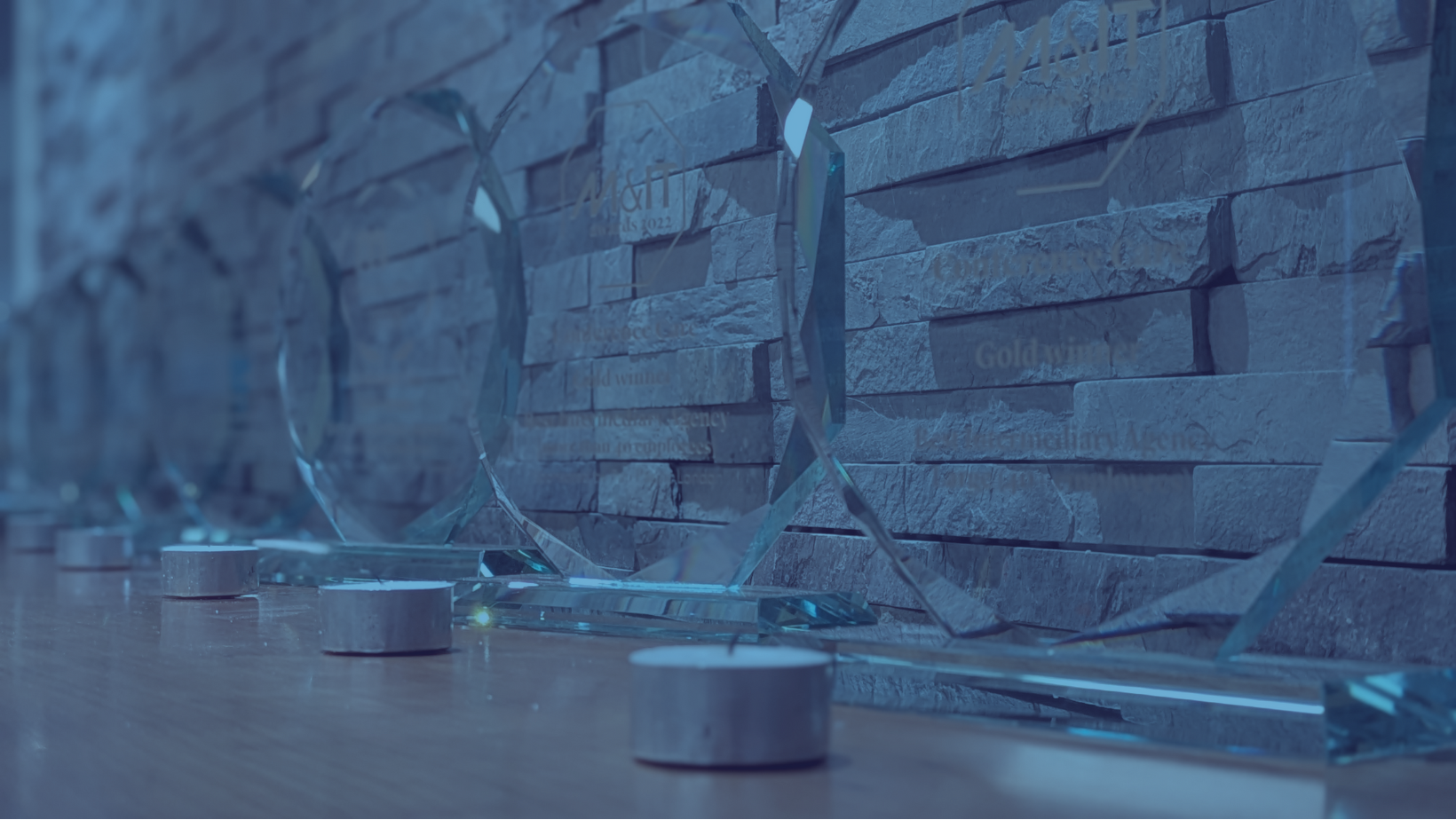 Blue Duotone image of M&IT awards lined on a desk
