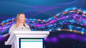 A woman stands behind a pedestal with a microphone in front of an AI background